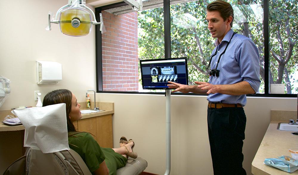 Dentist Explaining Treatment Options to a Patient - Volterra Dental Comprehensive and Aesthetic Dentistry Dentist explaining dental X-ray images to a patient in a modern dental office. - Volterra Dental Comprehensive and Aesthetic Dentistry